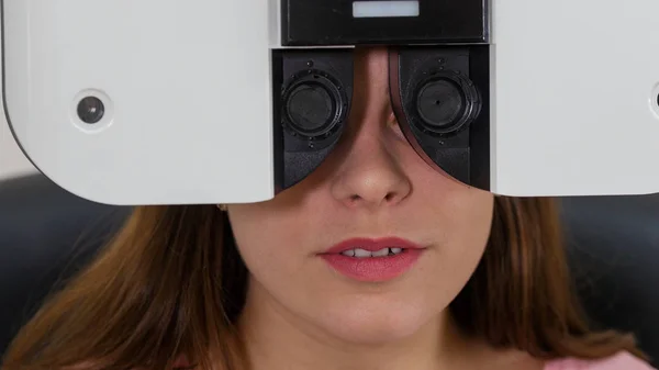 Szemészeti kezelés - egy fiatal nő ellenőrzi a látásélességét egy speciális szemészeti berendezéssel - egy gép lencsét cserél — Stock Fotó
