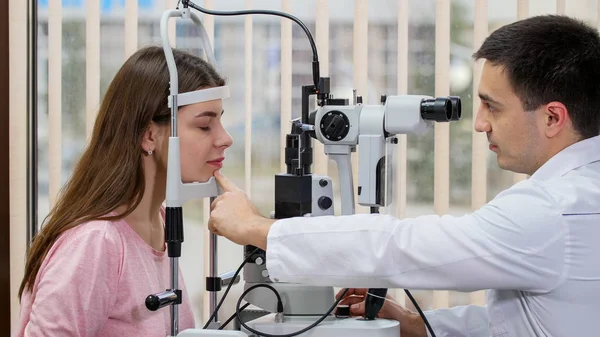 Augenärztliche Behandlung - junge hübsche lächelnde Frau überprüft ihre Sehschärfe mit einem Spezialgerät im hellen Schrank - legt ihr Kinn auf den Ständer — Stockfoto
