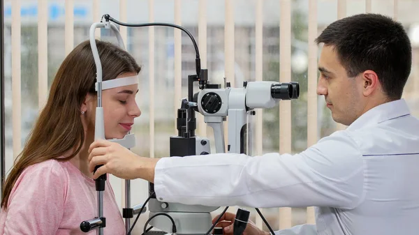Augenärztliche Behandlung - junge lächelnde Frau überprüft ihre Sehschärfe mit einem Spezialgerät im hellen Schrank - legt ihr Kinn auf den Ständer — Stockfoto