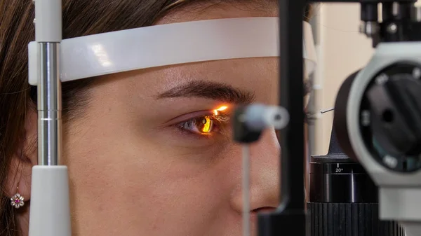 Augenheilbehandlung - eine junge Frau überprüft ihre Sehschärfe mit einem speziellen großen Optometriegerät - braune Augenfarbe — Stockfoto