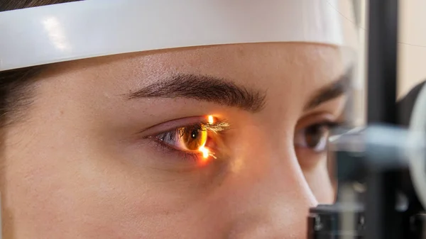 Une jeune femme vérifie son acuité visuelle avec une lumière d'une grande machine d'optométrie spéciale - couleur des yeux marron et sourcils soignés — Photo