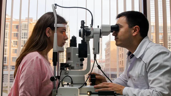 Ophthalmology treatment - young woman checking her visual acuity with a special equipment in the bright cabinet