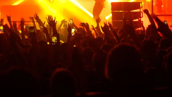 Energische Menschen, die beim Punk-Konzert mit erhobenen Händen tanzen - einige filmen den Auftritt mit dem Handy — Stockfoto