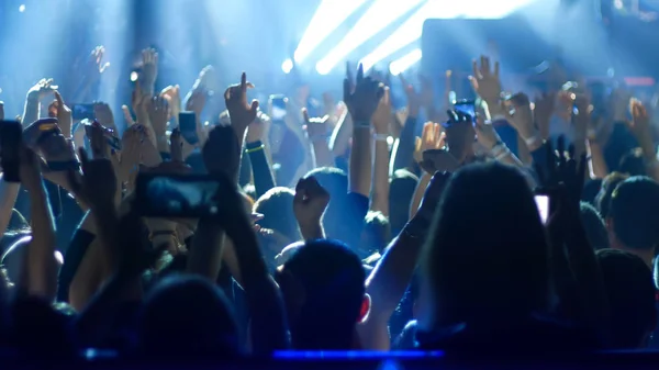 Energetische mensen dansen met hun handen omhoog bij het rockconcert - blauw licht — Stockfoto