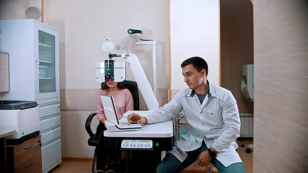Augenärztliche Behandlung - junge Frau überprüft ihre Sehschärfe mit einem optometrischen Gerät - ein Arzt sitzt in der Nähe — Stockfoto