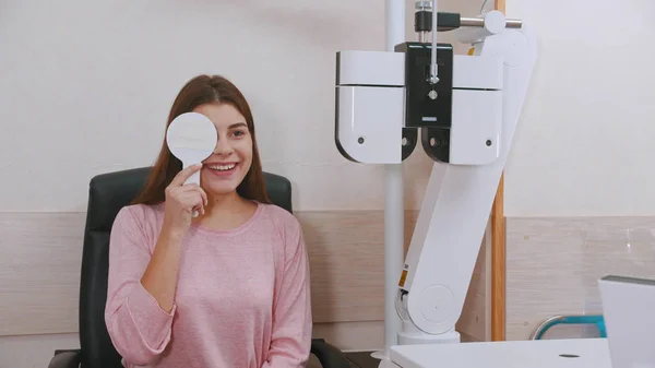 Augenheilkunde im Schrank - junge lächelnde Frau überprüft ihre Sehschärfe - Augen mit einem Augenschild schließen — Stockfoto