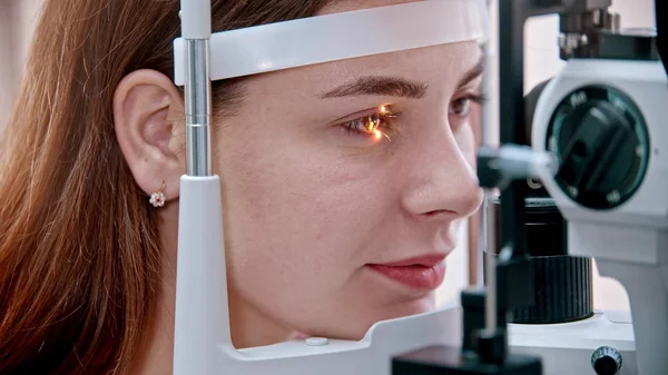 Tratamento oftalmológico - uma jovem mulher bonita verificando sua acuidade visual com uma luz da grande máquina especial de optometria - cor dos olhos castanhos — Fotografia de Stock