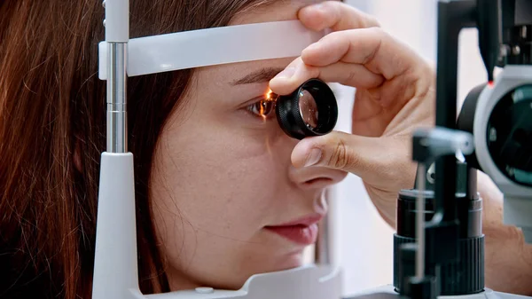 Ophthalmology treatment - a young woman checking her visual acuity with a light of special big optometry machine and lens - brown eyes color — 스톡 사진