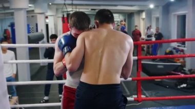 Spor salonunda boks antrenmanı. Ringde kavga eden iki atletik adam. Maçı izleyen başka bir adam.