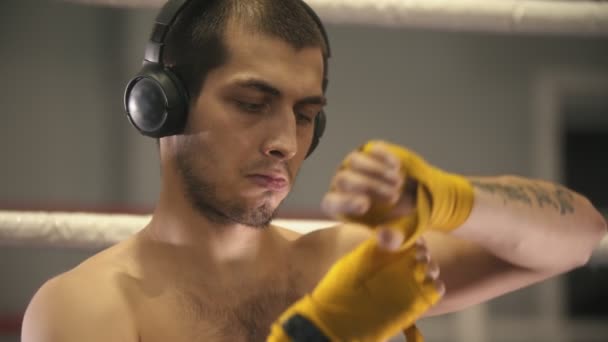盒装训练- -一个戴耳机的男人坐在拳击台的一角，用绷带包住双手 — 图库视频影像