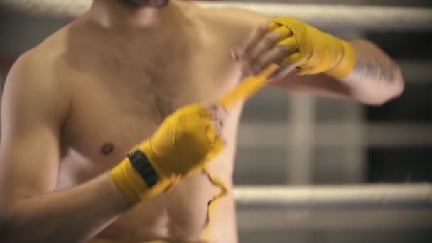 Box training - a man sitting on the corner of the ring and bandages his hands with an yellow band — Stock Video