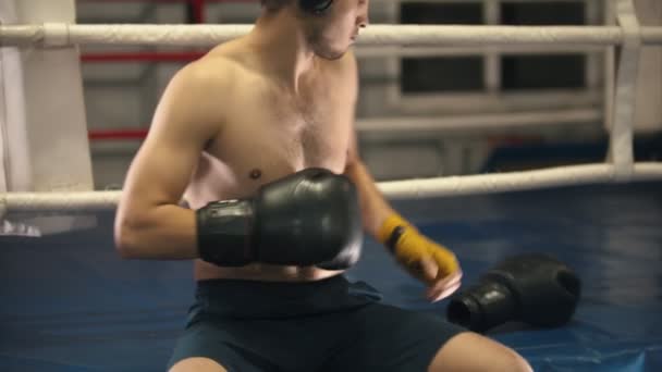 Entraînement en boîte - un homme tatoué assis sur le ring - portant écouteurs et gants — Video