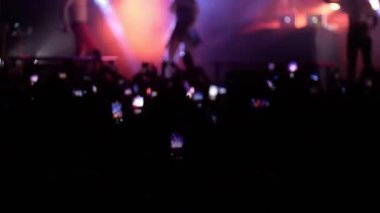 Rock konserinde elleri havada dans eden enerjik insanlar. Kışkırtıcı kostümlü bir kadın sahnede yürüyor.