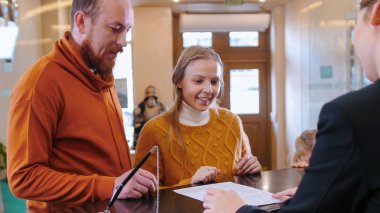 Oteli kontrol eden bir aile. Kiralık oda için evraklara bakan bir kadın.