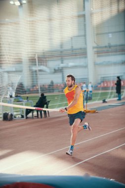Spor stadyumunda sırıkla atlama - pistte koşan sportif bir adam