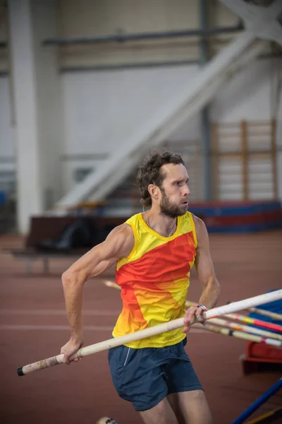 Skákání na tyči uvnitř - atletický muž běžící na trati s tyčí — Stock fotografie