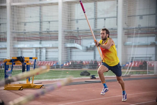 Stabhochspringen drinnen - ein athletischer Mann im gelben Hemd läuft auf der Bahn mit einer Stange im Stadion - rennt zum Sprung — Stockfoto