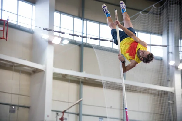 Pole vaulting indoors - a athletic man jumping over the bar — Stock Photo, Image