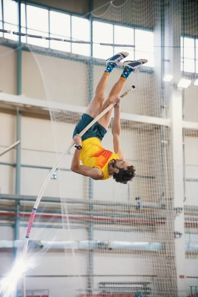 Pole vaulting indoors - a athletic man jumping over the bar - leaning on the pole — Stock Photo, Image