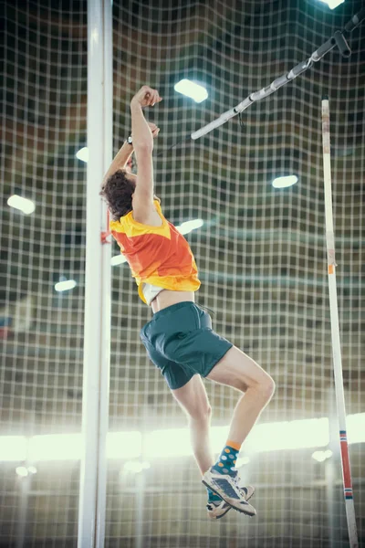 Bóveda de poste en el interior - un hombre deportivo que cae después del salto - luces brillantes en el fondo — Foto de Stock