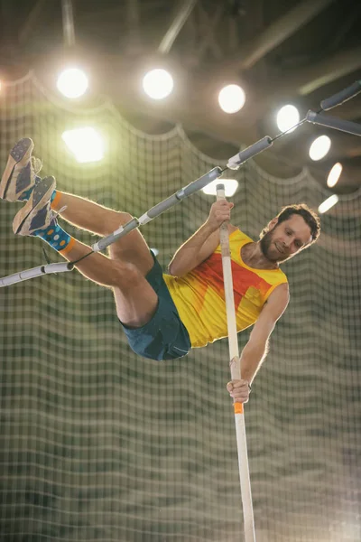 Stabhochsprung im Sportstadion - ein athletisch lächelnder Mann im gelben Hemd springt über die Stange — Stockfoto