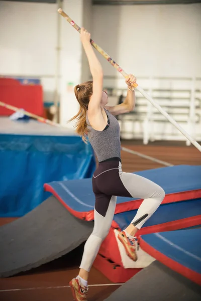 Pole bóveda en el estadio de deportes - joven mujer deportiva con cola de caballo en gris leggins a punto de saltar por encima de la barra — Foto de Stock