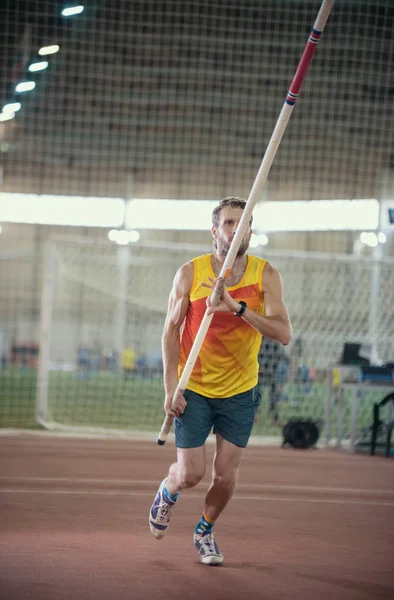 Pole vaulting in the sports stadium - an athletic man in yellow shirt running on the track — Stock Photo, Image