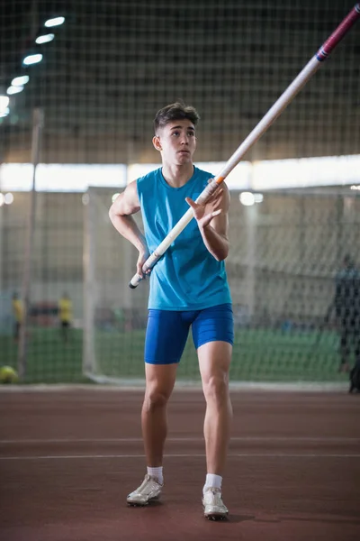 Pole vault training in the sports stadium - νεαρός άνδρας στέκεται στην πίστα κρατώντας ένα κοντάρι και κοιτάζοντας προς τα πάνω — Φωτογραφία Αρχείου