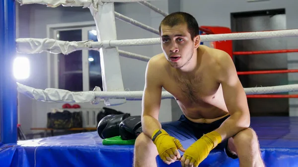 Box - bokser zet zijn ellebogen op zijn knieën en zit naast de ring — Stockfoto
