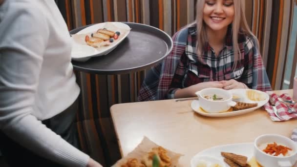 Una mujer camarera trae comida a una pareja junto a la mesa — Vídeo de stock