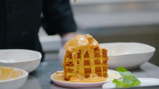 Cocina del restaurante - Verter una salsa dulce y granola en la parte superior de la torta de miel — Vídeos de Stock