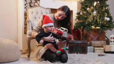 Küçük bebeğiyle Noel stüdyosunda oynayan genç bir kadın.