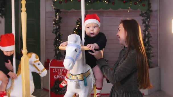 Conceito de Natal - Dois bebês sentados em cavalos de carrossel e brincando com eles — Vídeo de Stock