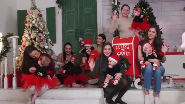 Рождественская концепция - несколько женщин-матерей, держащих своих детей в руках в оформленной студии - машут руками — стоковое видео