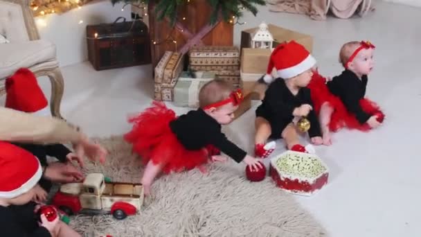 Concepto de Navidad - Pequeños bebés sentados en la alfombra y jugando con pelotas y juguetes de Navidad en el estudio decorado — Vídeos de Stock