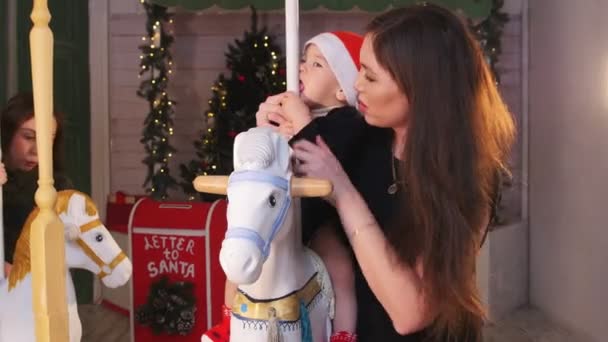 Conceito de Natal - Dois bebês sentados em cavalos de carrossel dentro de casa e brincando com eles — Vídeo de Stock