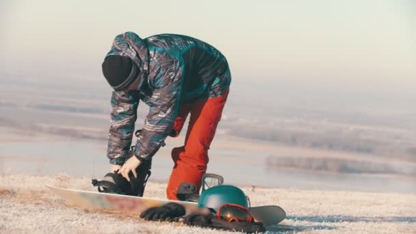 Koncepcja snowboardu - sportowiec z protezą nogi stojący na desce i zakładający na nią buty — Wideo stockowe