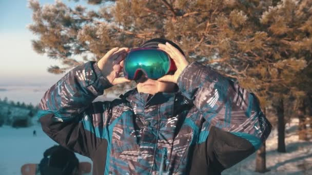 Snowboarding - A smiling man snowboarder putting on protective glasses — Stock Video
