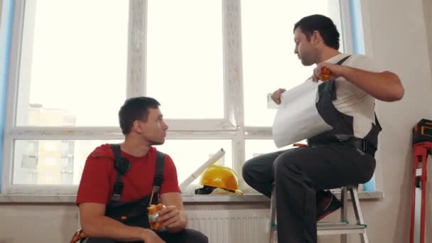 Ремонт квартиры - проект квартиры - мужчины рабочие сидят на подоконнике и обсуждают план во время перерыва — стоковое видео