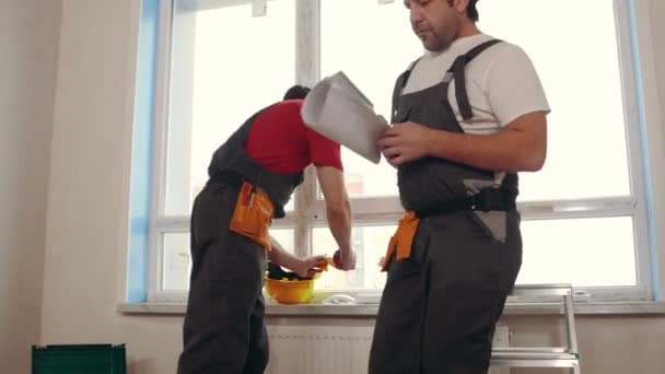 Проект квартиры - мужчины рабочие встают с подоконника и начинают работать по плану — стоковое видео