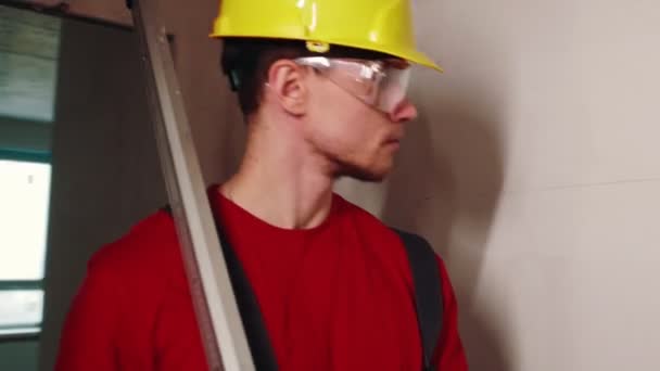 Projet appartement - un travailleur homme en casque jaune marchant sur la zone tenant une barre de mesure — Video