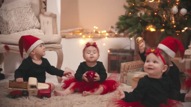Weihnachtsdekoration im Atelier - kleine Babys sitzen auf dem Boden im Weihnachtsatelier und spielen mit Spielzeug — Stockvideo