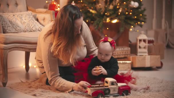 Jul - En kvinna leker med sin lilla dotter med en julboll och leksaksbil — Stockvideo