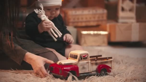Julkoncept - En ung kvinna leker med sin lilla bebis i julateljén - en bebis som håller i leksaksrådjur och en billeksak — Stockvideo