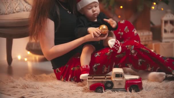Різдвяна концепція - жінка тримає свого маленького сина - дитину, яка грає з золотим різдвяним м'ячем — стокове відео