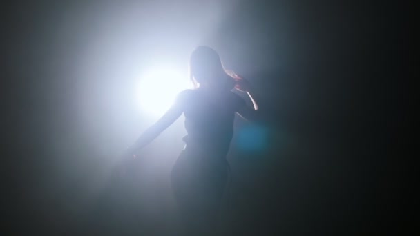 Silhouette de gracieuse jeune femme dansant dans un studio sombre 