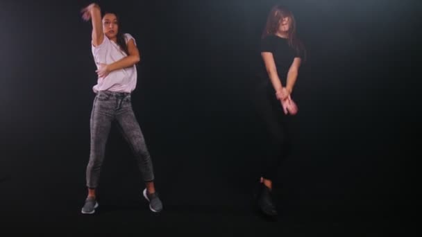 Two young women freestyle dancing in dark studio — Stock Video