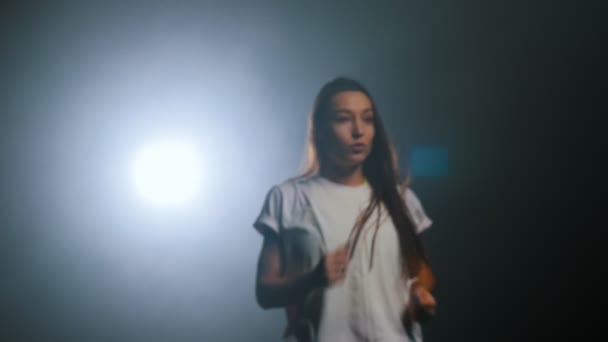 Junge Frau tanzt und geht im dunklen Studio ans Licht — Stockvideo