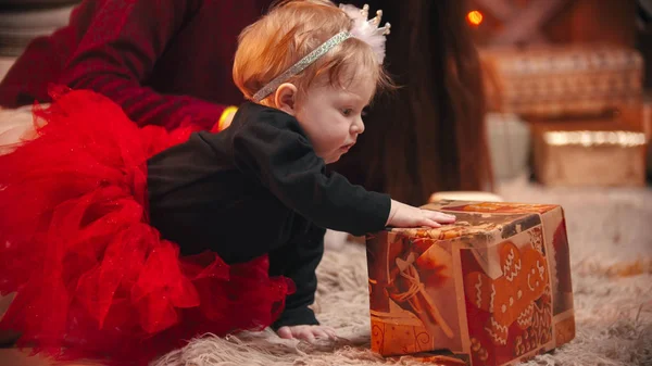 Christmas concept - A cute little baby with a bow on the rim playing with a gift box — ストック写真