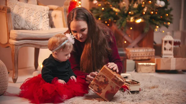 Concepto de Navidad: una mujer sentada en el estudio con su hija pequeña y jugando con una caja de regalo — Foto de Stock